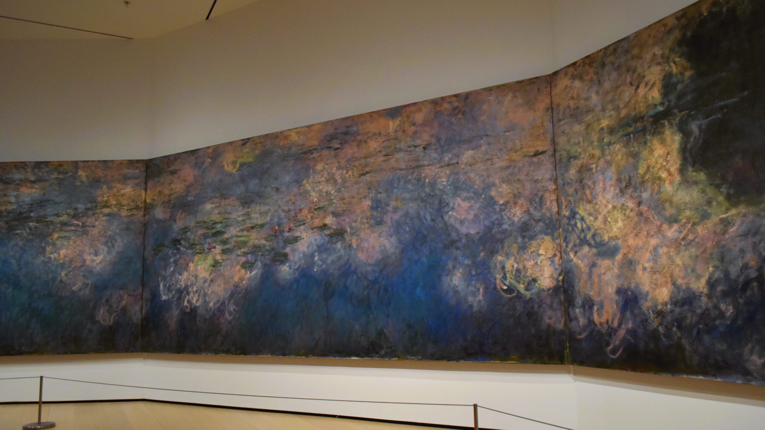 Experience the panoramic view of Monet's water lilies painting at the Museum of Modern Art in New York, where it graces a gallery with elegant wooden floors.