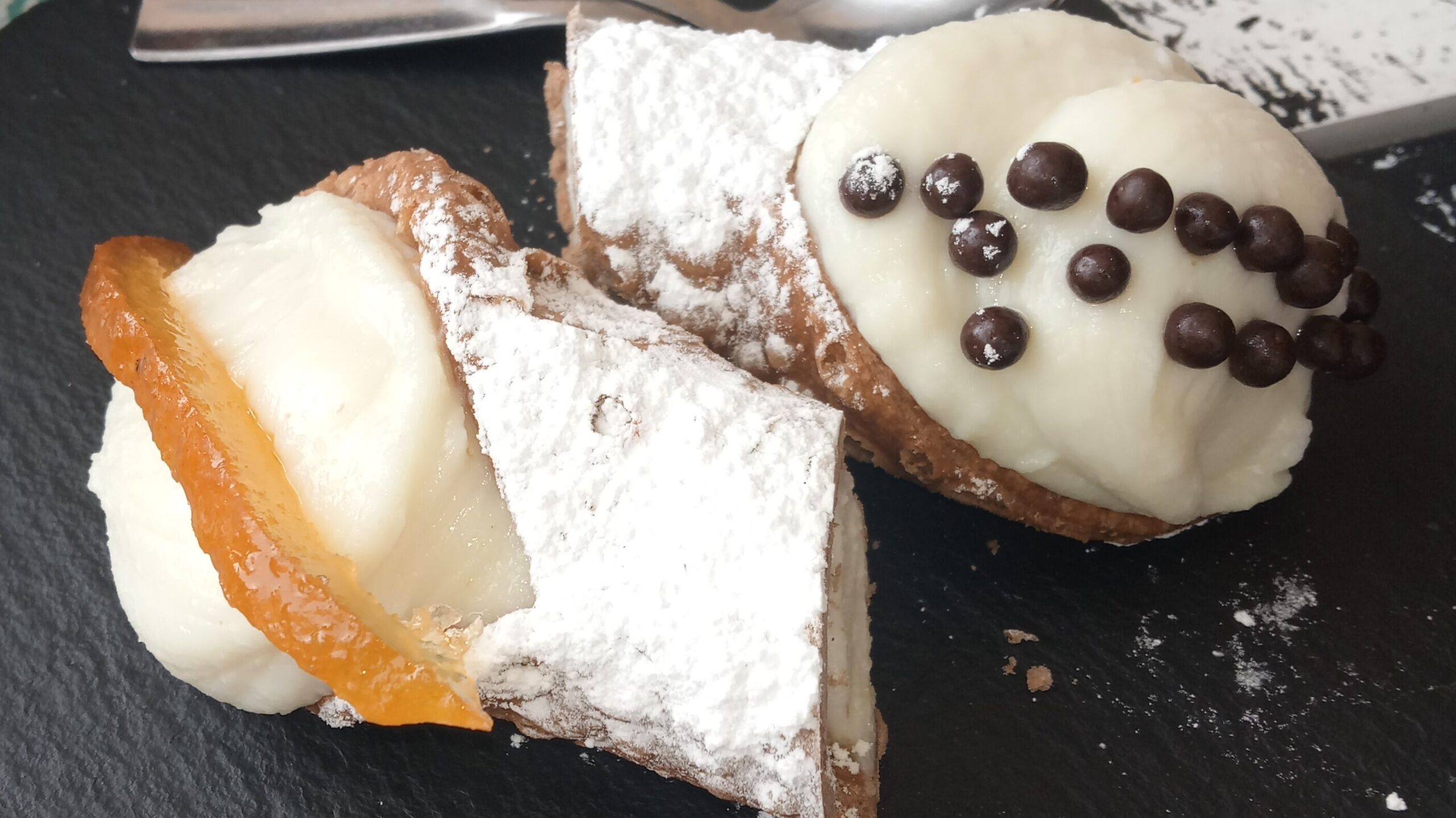 Cannoli on a slate plate stands out as the best Italian food, filled with cream and garnished with chocolate chips and candied orange.