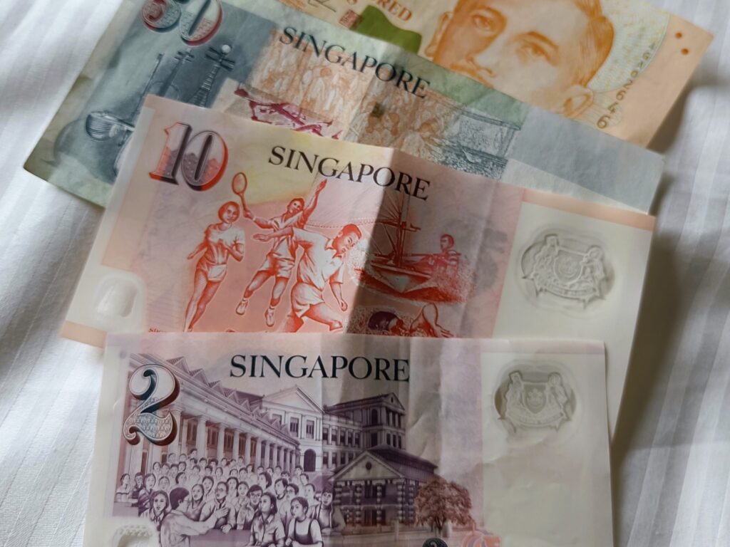 Five Singaporean banknotes in various denominations laid out on a white fabric surface, perfect for those experiencing Singapore for the first time and seeking essential tips on local currency.