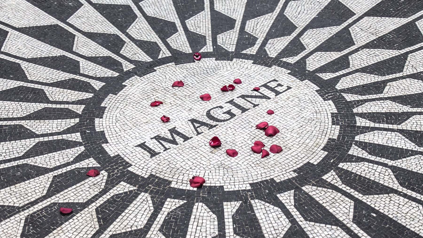 A red rose is placed in the middle of a mosaic floor with the word imagine.