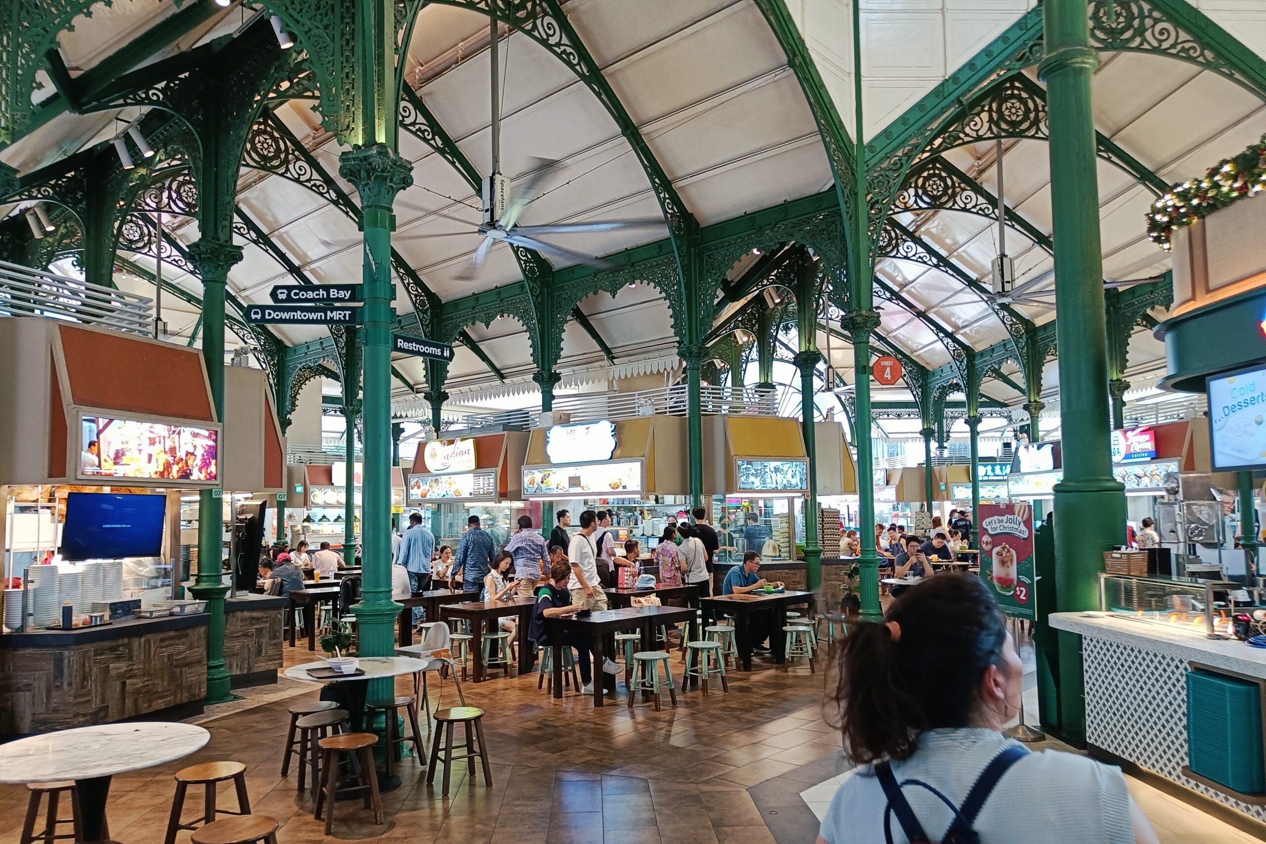 Experiencing the bustling indoor food market in Singapore for the first time, you'll find people dining amidst ornate green metal pillars. Don't miss these essential tips to make the most of your visit!.