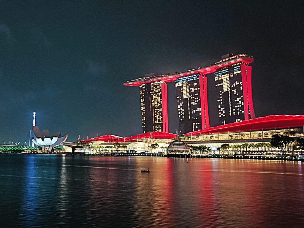 Night view of Marina Bay Sands, one of the most popular attractions in Singapore, illuminated in red and reflecting beautifully on the water.