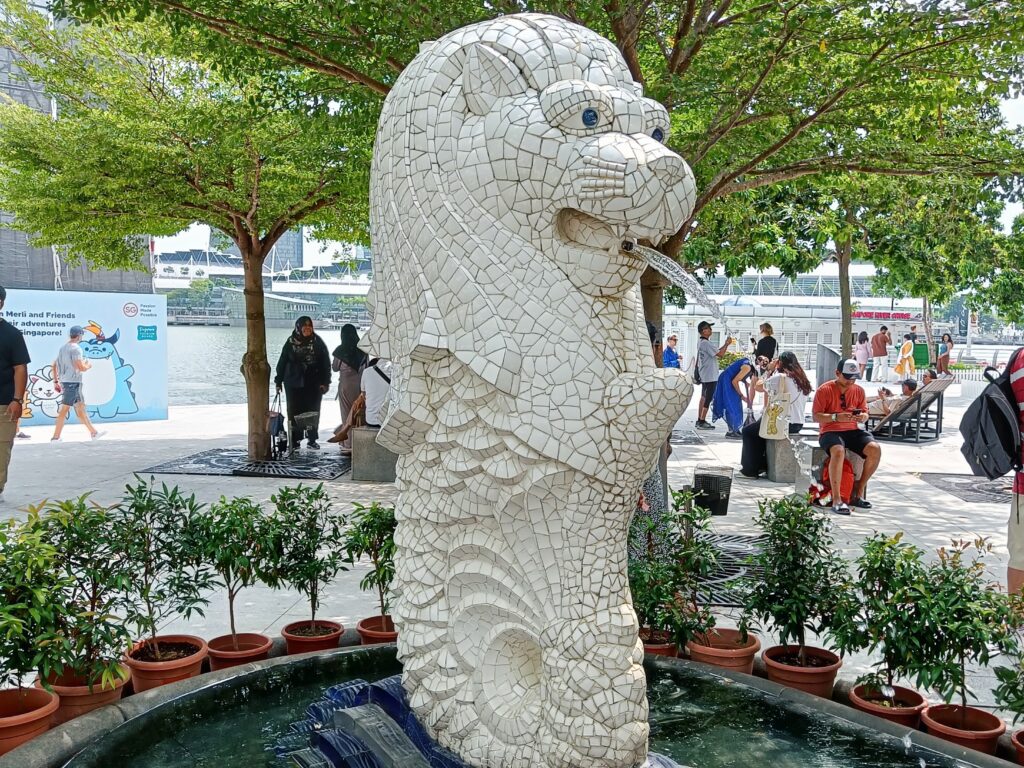 A mosaic Merlion statue, one of the most popular attractions in Singapore, stands majestically in a park surrounded by lush trees and bustling people.