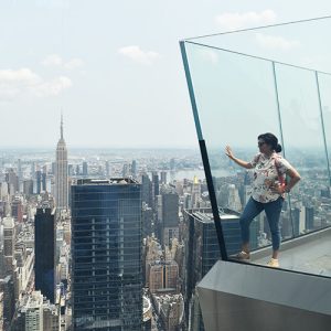 Person standing on a glass platform with a city skyline and skyscrapers in the background.