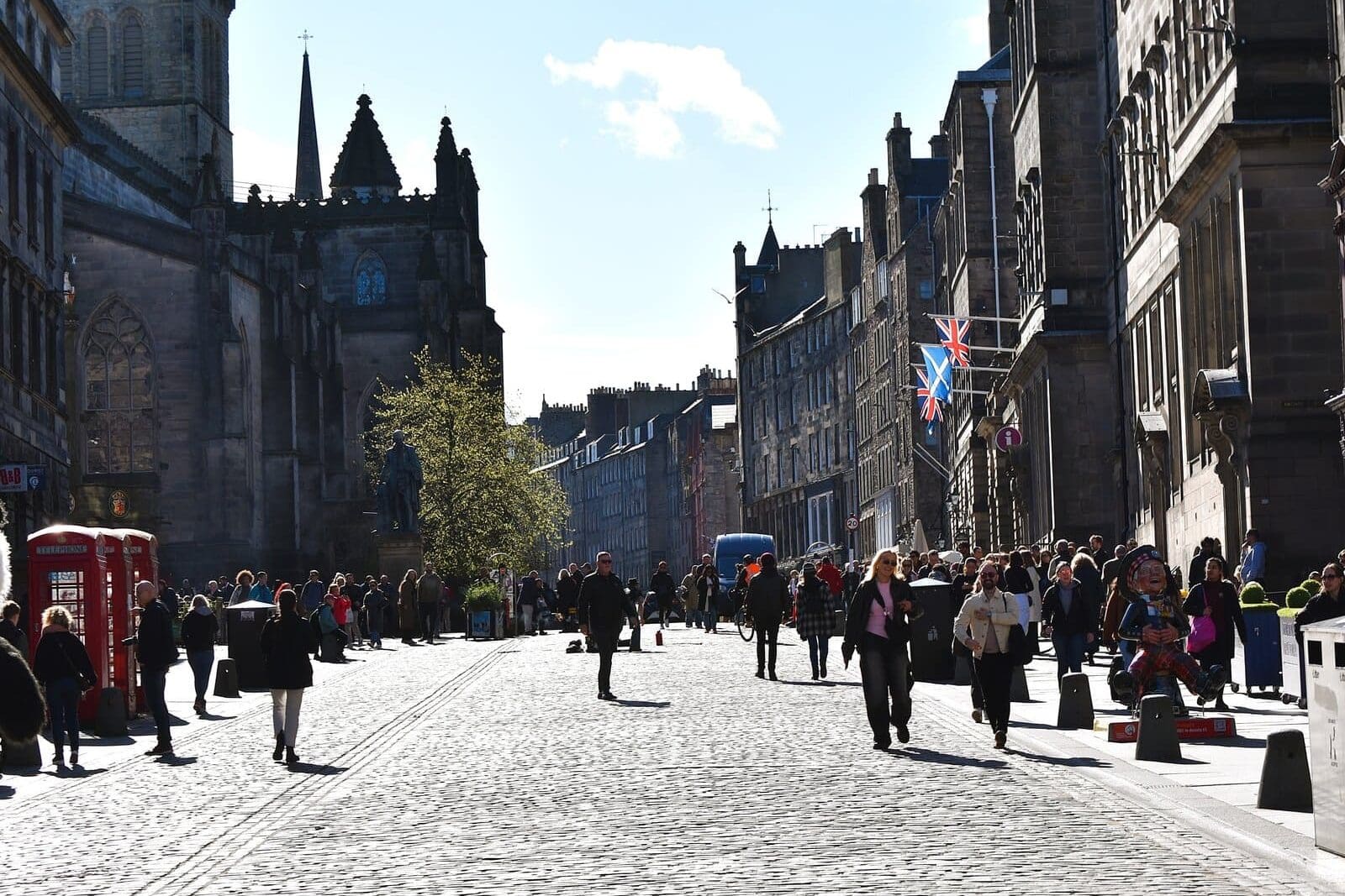 People walking along a cobblestone street lined with historic buildings take in some of the best attractions Edinburgh has to offer on a sunny day.