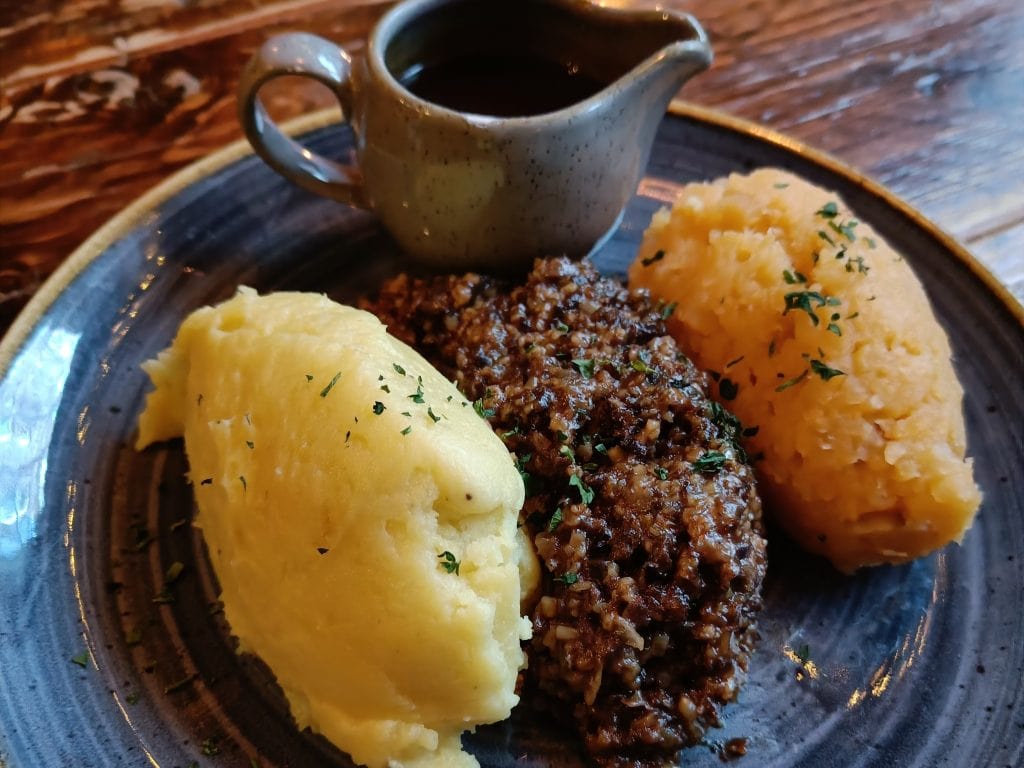 A plate with mashed potatoes, haggis, mashed turnips, and a small jug of gravy on a rustic table—perfect for savoring during your Edinburgh travel or as part of a classic 2 days in Edinburgh itinerary.