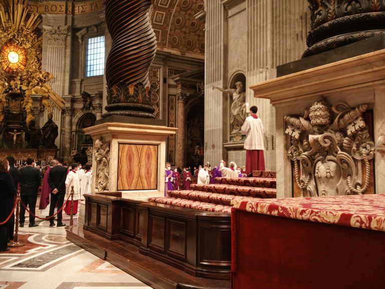 Clergy in ceremonial robes gather inside an ornate church with marble columns and decorative details, marking festive dates in Rome.