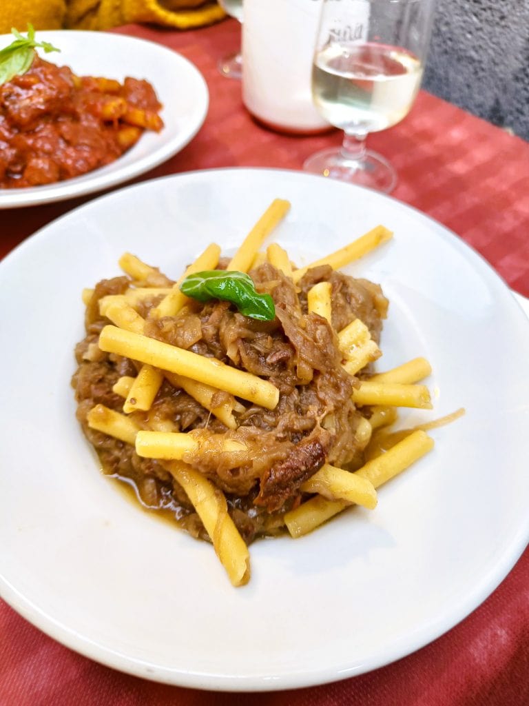 A plate of pasta with shredded meat sauce, topped with a basil leaf, on a red tablecloth—a classic example of Naples cuisine and a must try food Naples is famous for.
