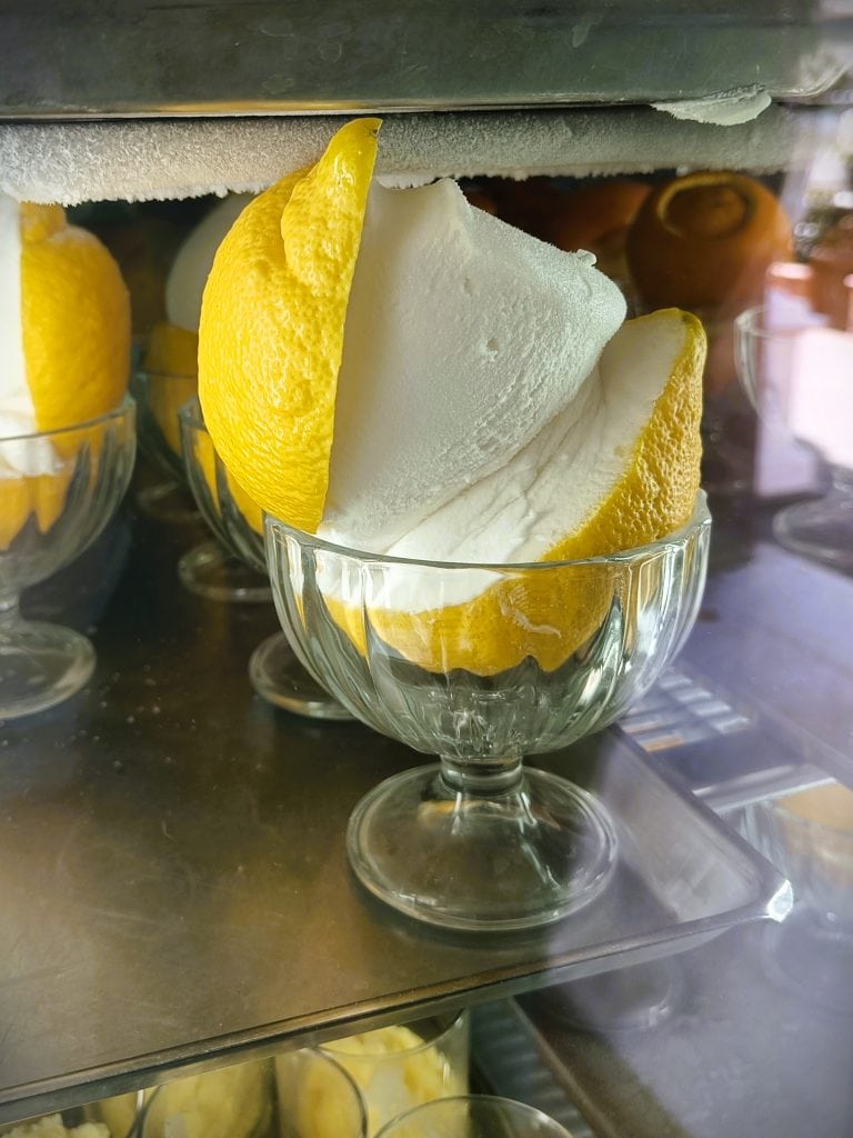 A glass cup holds lemon sorbet served inside a hollowed-out lemon half—a refreshing nod to Naples cuisine and one of the must-try dishes Naples is famous for.