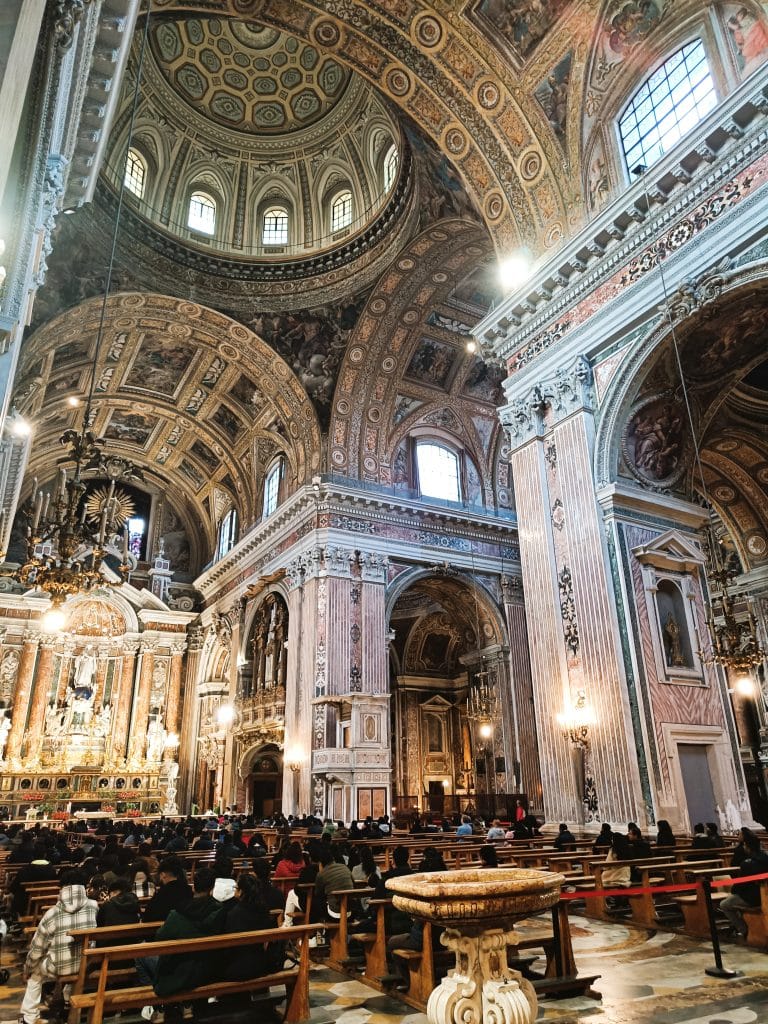 People seated inside an ornate, grand cathedral with high domed ceilings and intricate architectural details—truly one of the top Naples attractions for those interested in stunning architecture and memorable Naples sightseeing.