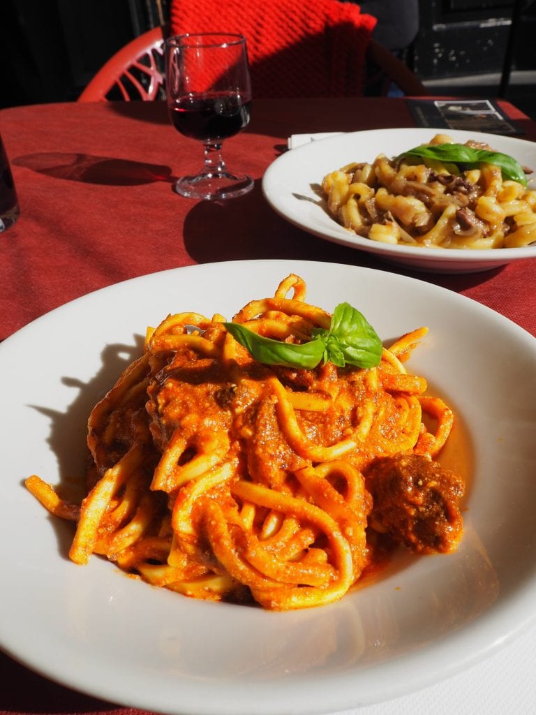 Two plates of pasta on a red tablecloth showcase must-try Naples food: one with tomato sauce and meatballs, the other with a creamy sauce—classic examples of Naples cuisine.