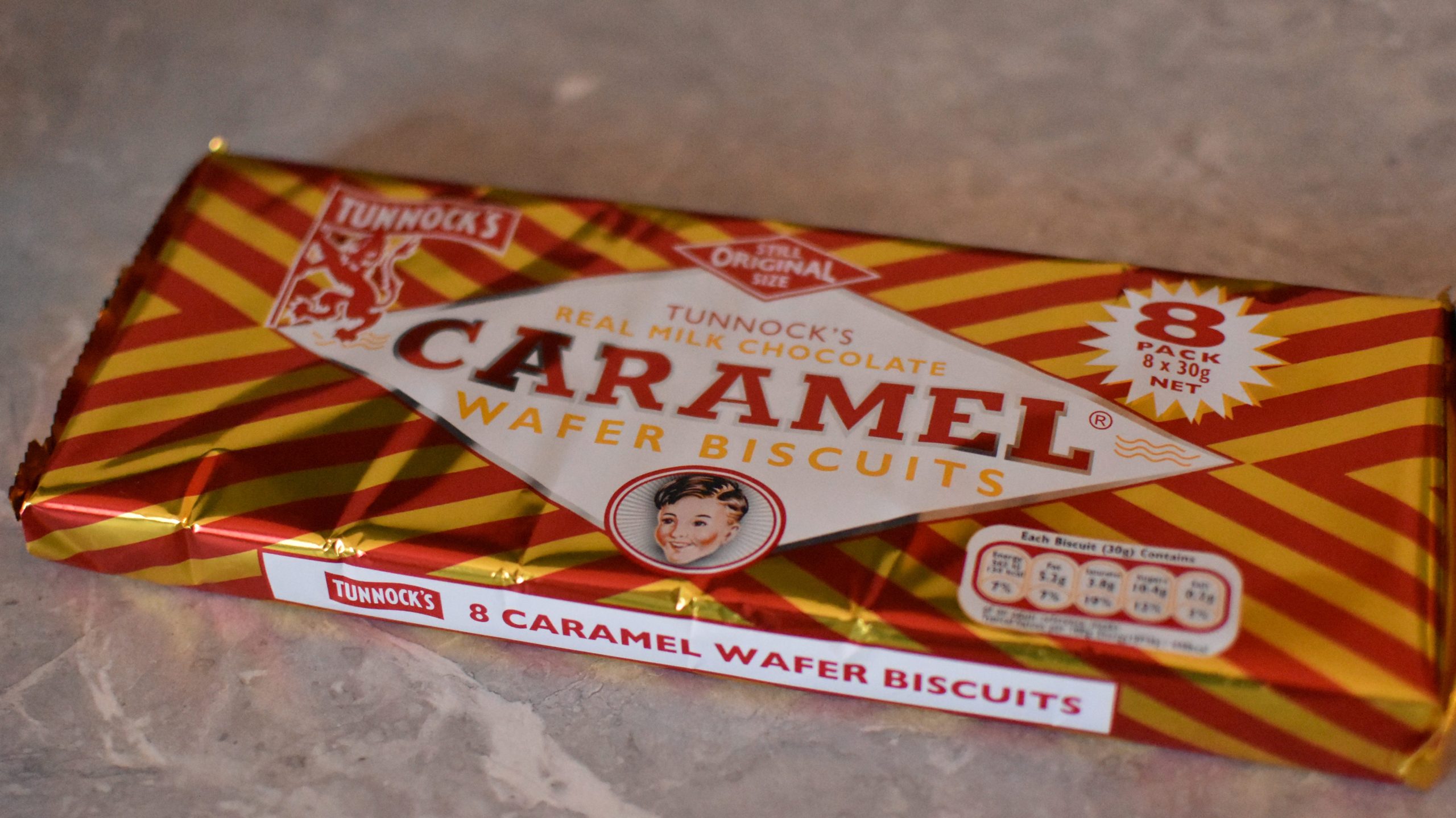 A pack of Tunnock's Caramel Wafer Biscuits, a classic Glasgow treat and popular food souvenir, sits on a gray surface with its signature red and yellow striped wrapping.