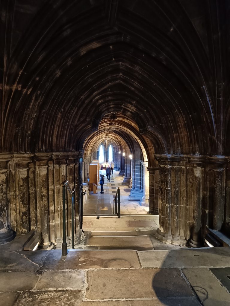 Stone arched hallway with people in the distance, illuminated by natural light from arched windows—capturing the timeless charm featured in many “10x Best things to do in Glasgow” guides.