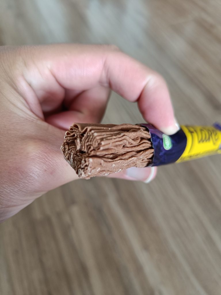 A hand holding a partially unwrapped, textured chocolate bar—one of the best Food souvenirs from Glasgow—over a wooden floor background.