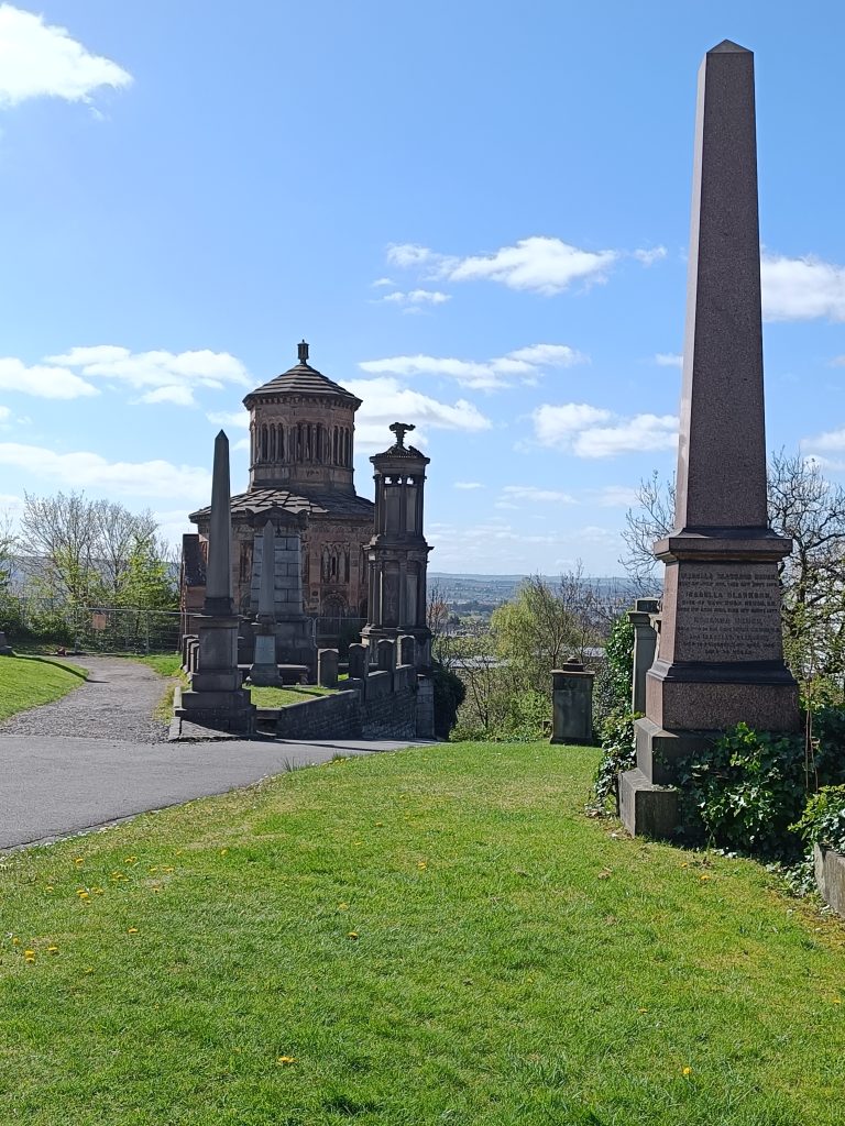 A grassy path leads to a historic mausoleum and tall stone obelisks under a bright blue sky—one of the 10x Best things to do in Glasgow for history lovers and explorers alike.