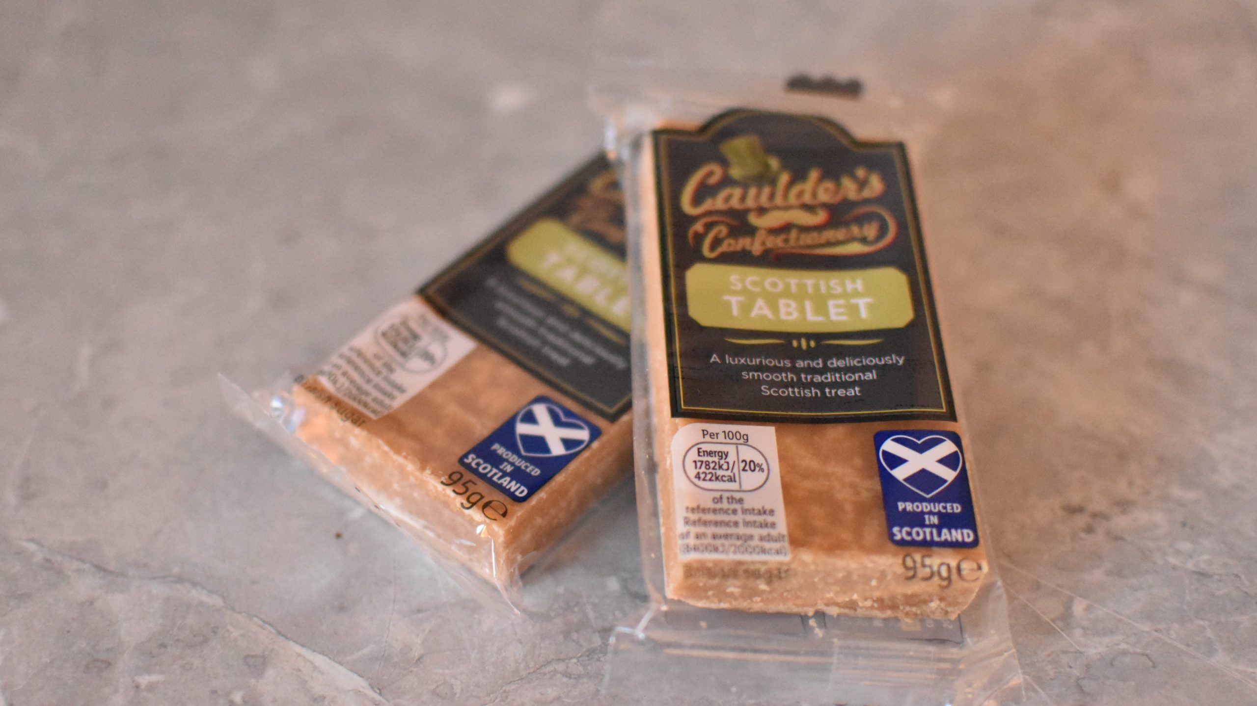 Two wrapped bars of Scottish tablet on a grey surface, each labeled as a traditional Scottish treat—perfect food souvenirs from Glasgow.