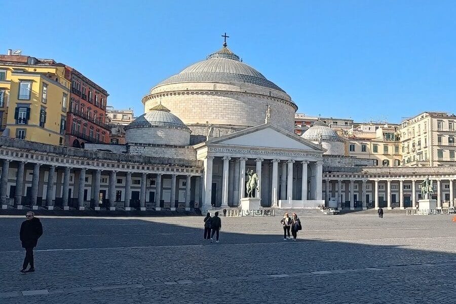 Wide plaza with people walking, a domed church, columns, and colorful buildings under a clear blue sky—this vibrant scene captures the essence of one of 6x Popular neighborhoods in Naples