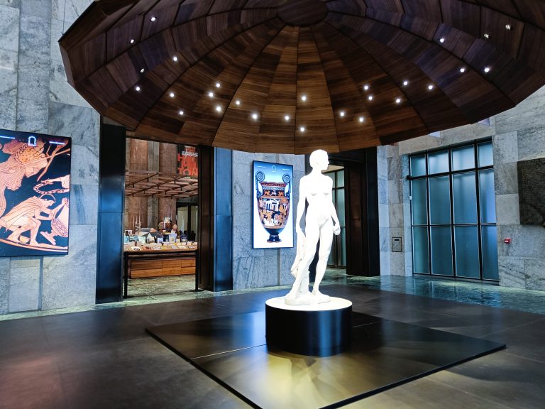 White statue under wooden dome with spotlights, flanked by art panels in a modern marble lobby—an elegant highlight among the best museums in Naples and a must-see for anyone exploring top Naples attractions.