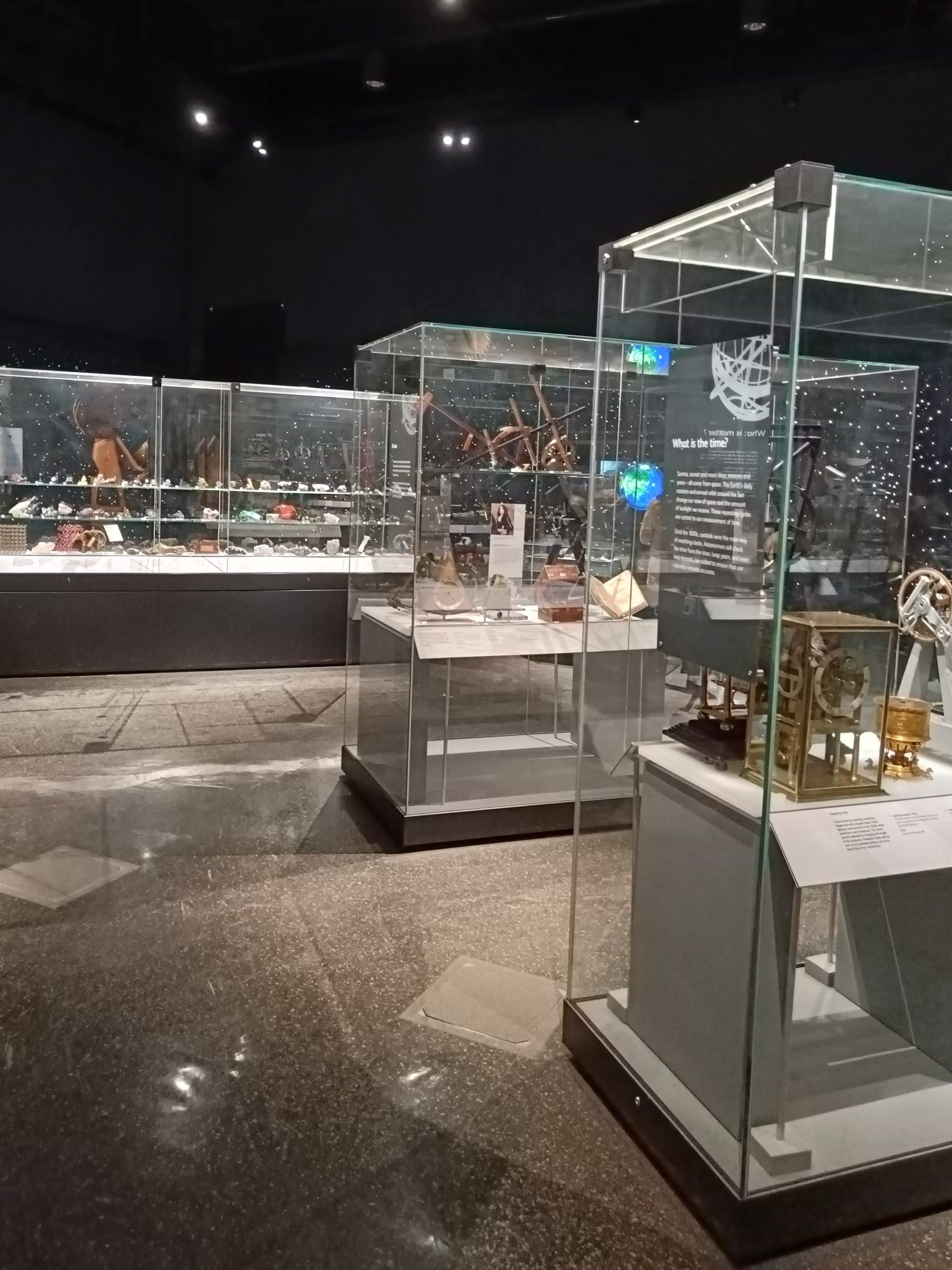 Glass display cases with various artifacts and objects in a dimly lit museum exhibition room await those who visit the National Museum of Scotland.