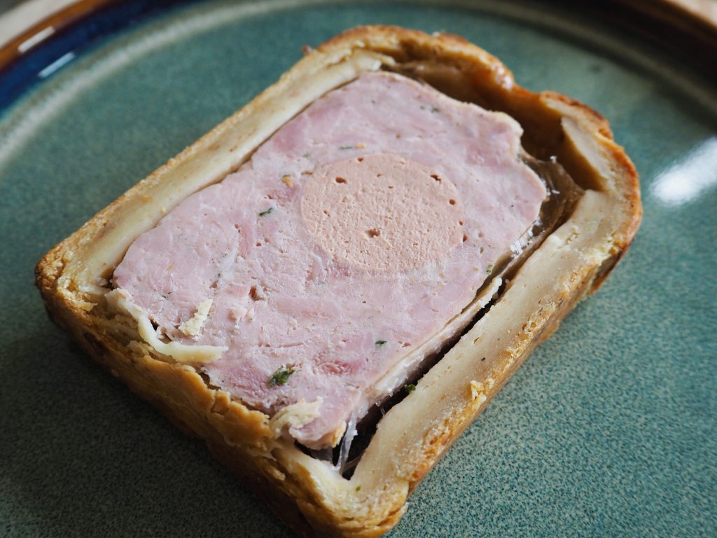 A slice of pâté en croûte with layers of meat and pastry on a green plate.