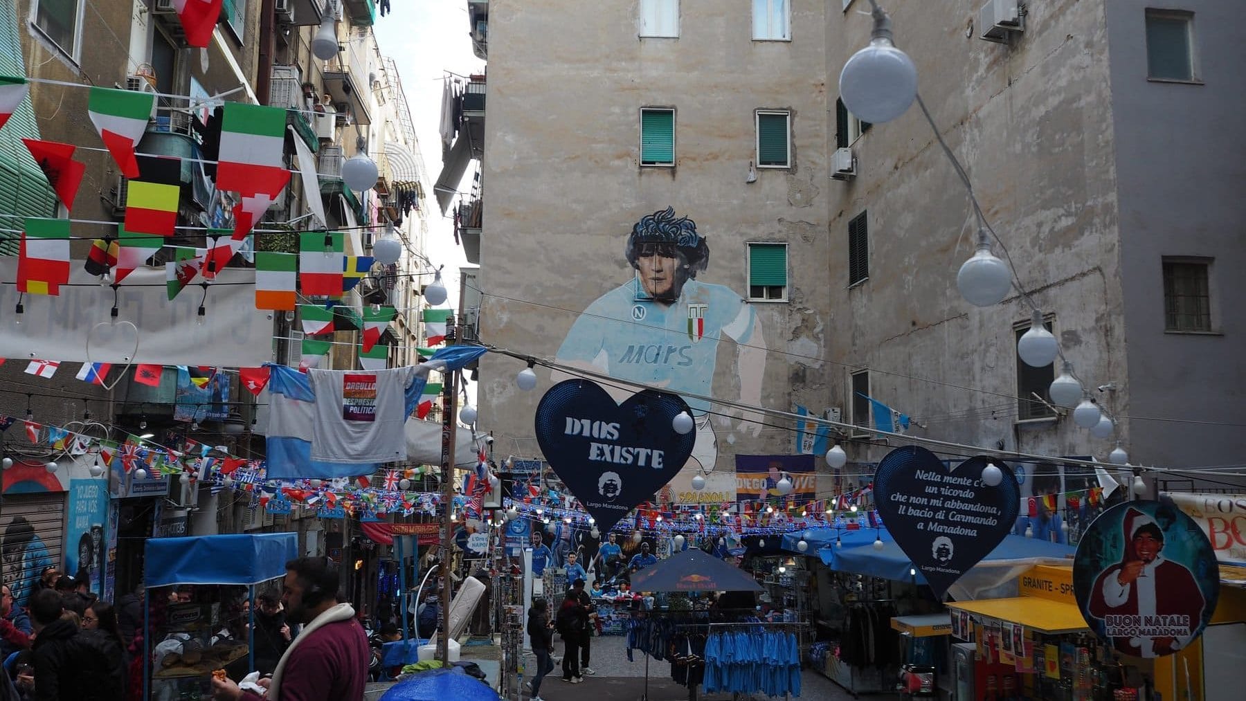 Street market decorated with flags and a large mural of Diego Maradona on a building wall—one of the best attractions Naples has to offer and a must-see for anyone looking for authentic things to do in Naples.