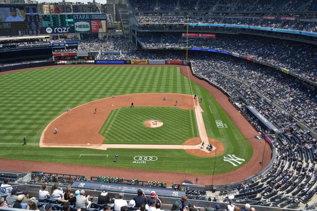 Aerial view of a baseball game in progress at a crowded stadium in one of the vibrant boroughs of New York City on a sunny day.