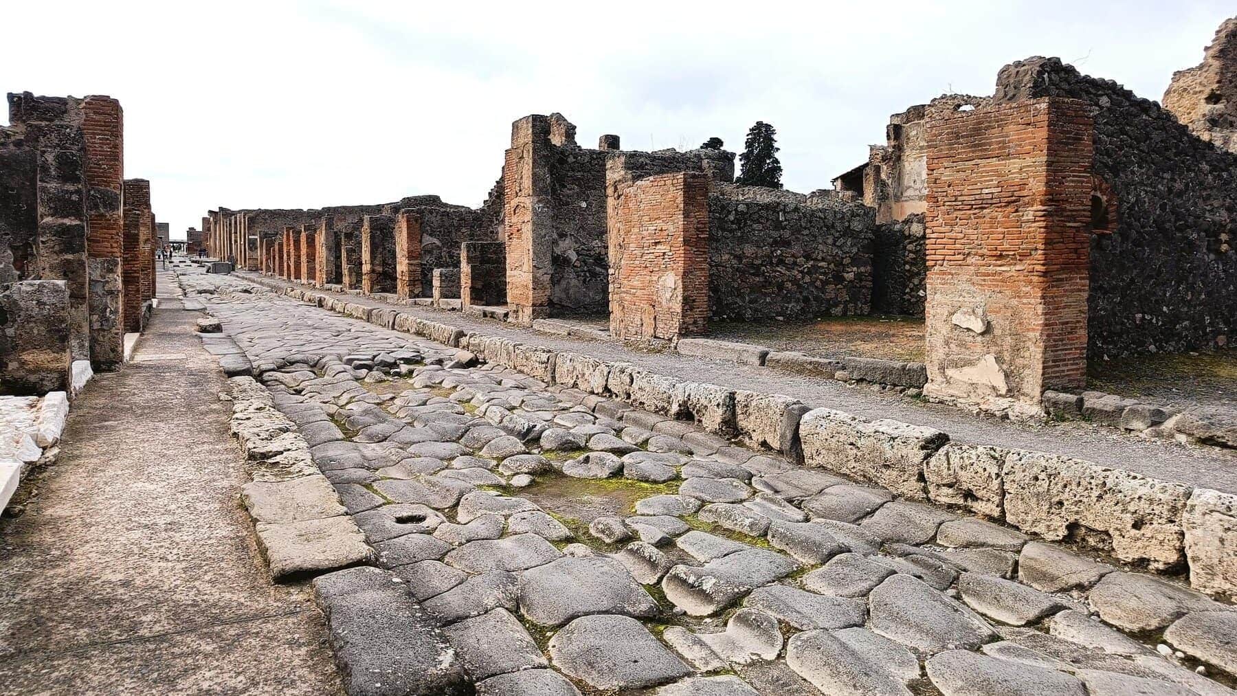 Ancient stone street lined with ruins of brick buildings in the archaeological site of Pompeii, one of the best attractions Naples has to offer for history lovers.
