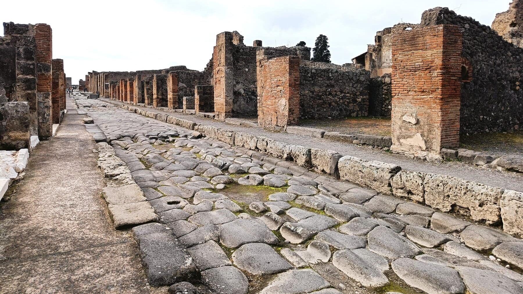 Ancient stone street lined with ruins of brick buildings in the archaeological site of Pompeii, one of the best attractions Naples has to offer for history lovers.