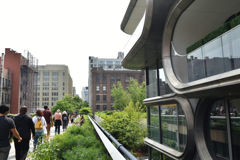 People walking along a green, elevated urban park with modern and older buildings in the background—visit the High Line for this unique blend of city views and nature.