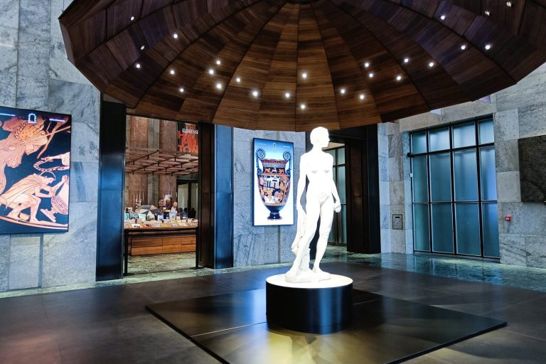 White statue under wooden dome with spotlights, flanked by art panels in a modern marble lobby—an elegant highlight among the best museums in Naples and a must-see for anyone exploring top Naples attractions.