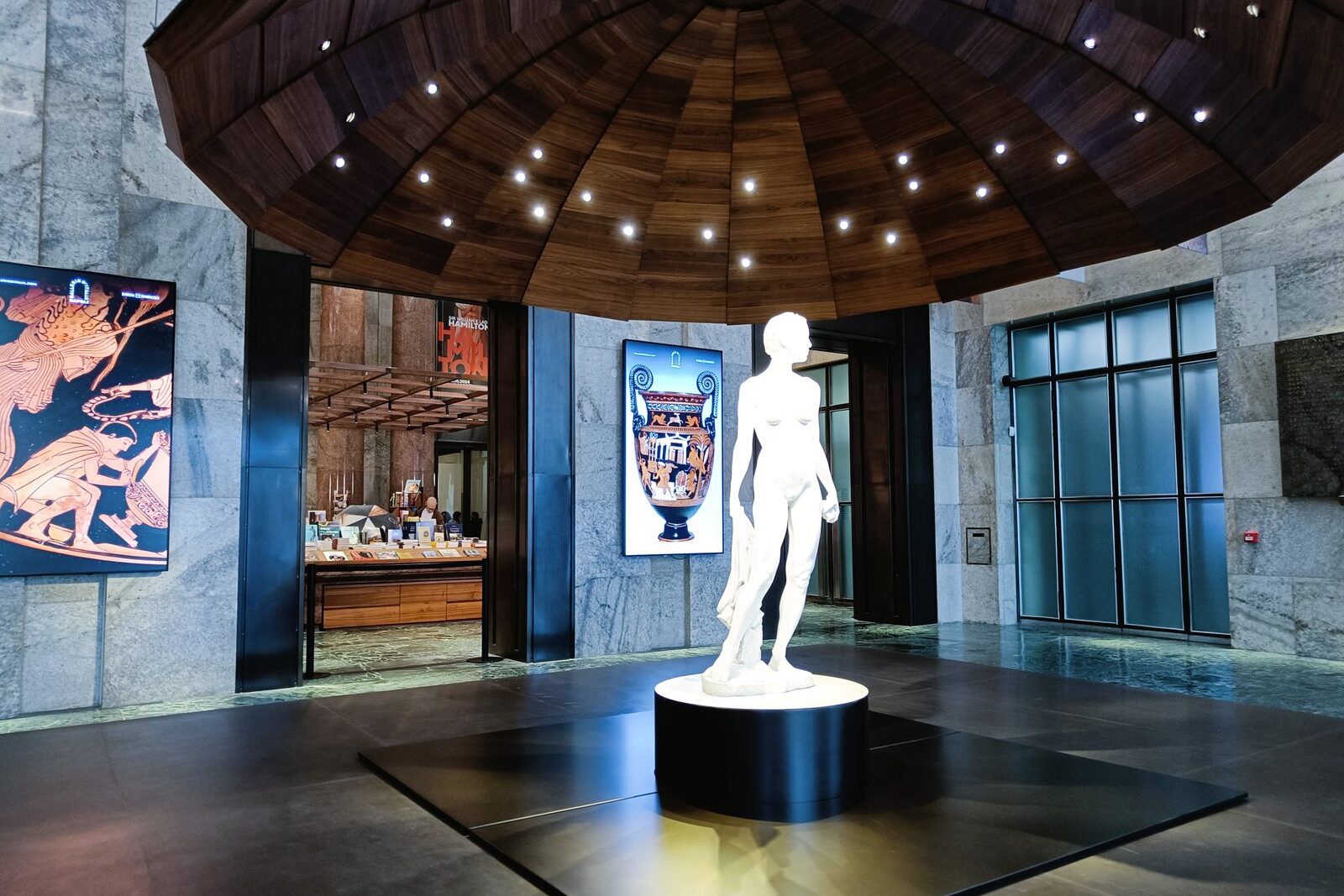 White statue under wooden dome with spotlights, flanked by art panels in a modern marble lobby—an elegant highlight among the best museums in Naples and a must-see for anyone exploring top Naples attractions.