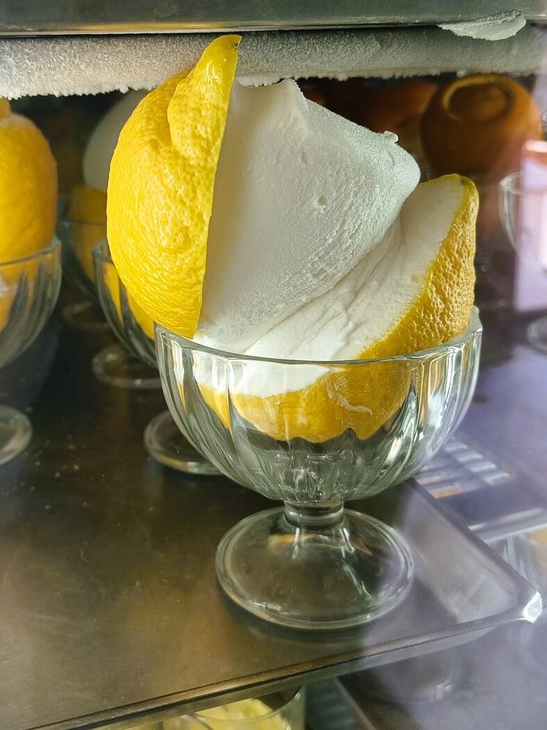 A glass cup holds lemon sorbet served inside a hollowed-out lemon half—a refreshing nod to Naples cuisine and one of the must-try dishes Naples is famous for.