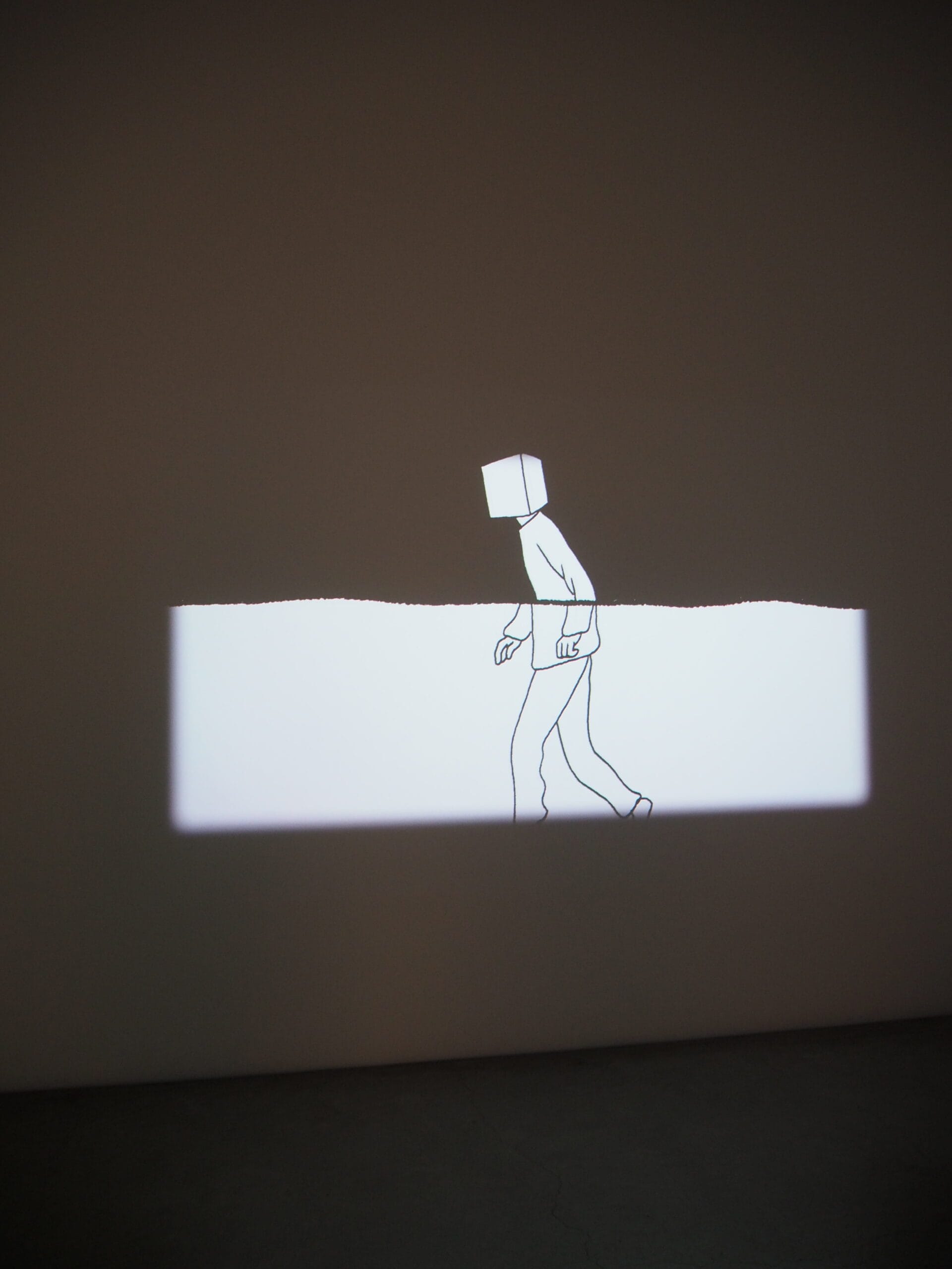 A line drawing of a person with a box head is projected on a wall, half obscured by a white horizontal band.