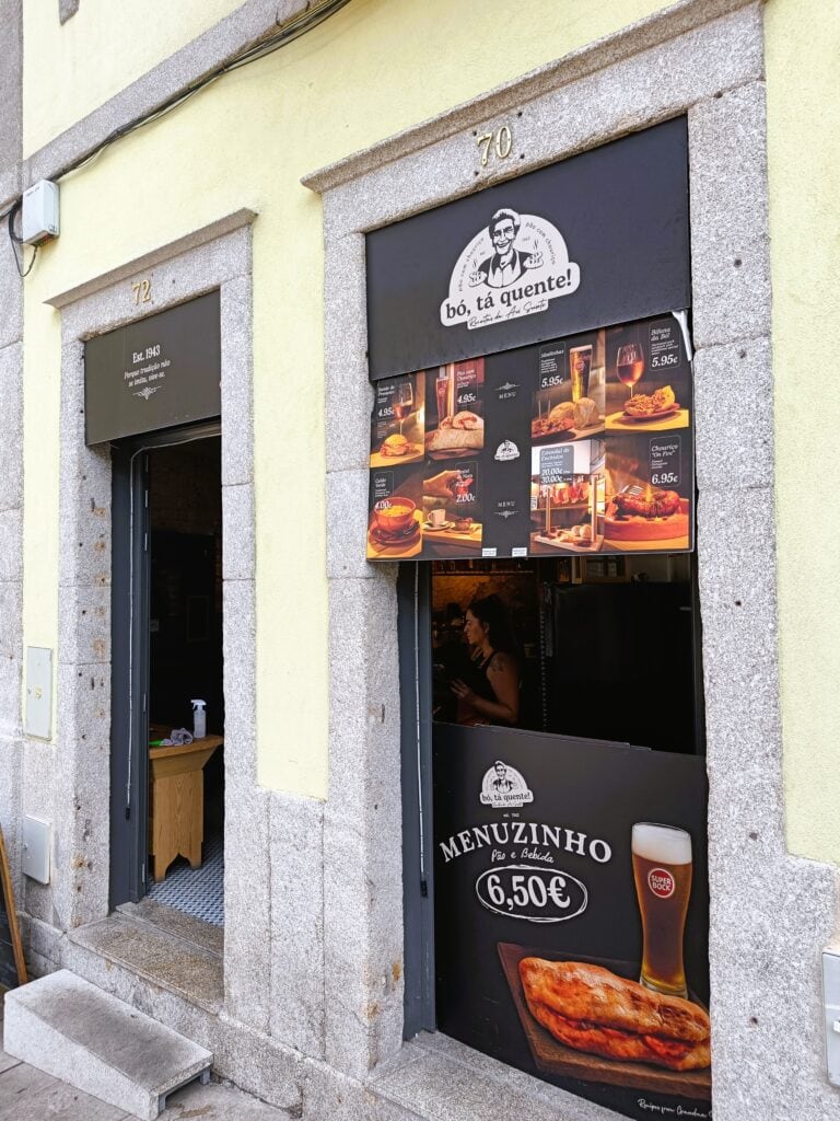 Yellow building with open door and food posters above a window advertising a €6.50 menu with beer and sausage—a tasty spot if you're wondering where to eat in Porto.
