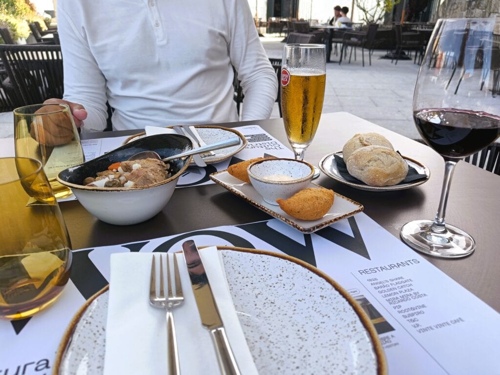 A meal of stew and appetisers is served with beer and wine on an outdoor terrace—a perfect spot if you’re wondering where to eat in Porto.