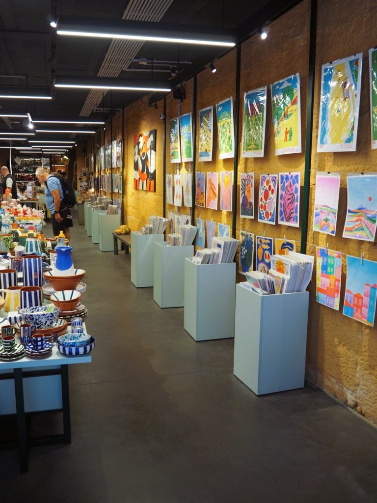Art gallery with colourful paintings on the wall and ceramic items displayed on tables, drawing people browsing—one of the popular attractions in Porto for art lovers.
