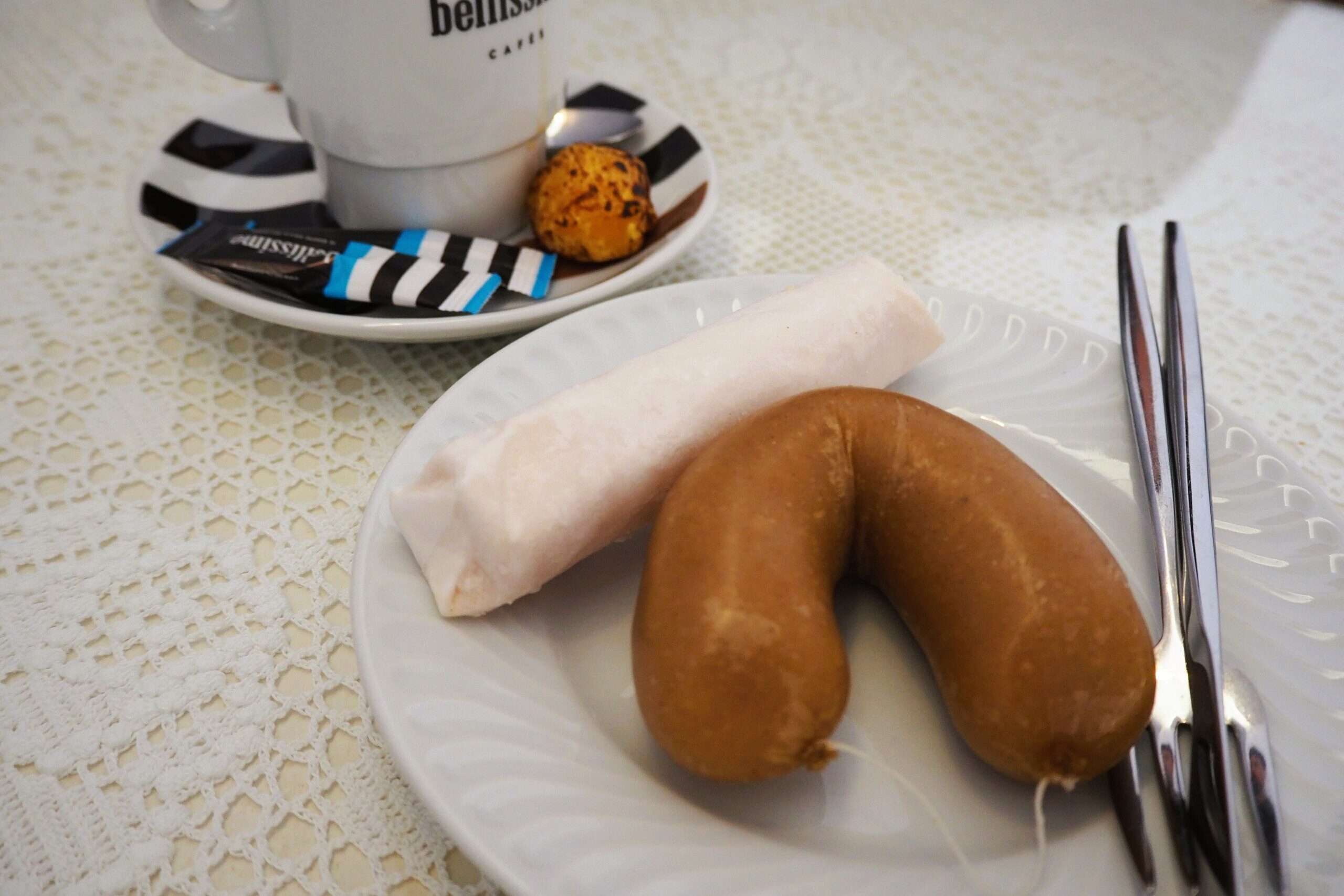A white plate with two sweets and two forks next to a cup of coffee on a lace tablecloth, showcasing some of the best food Porto has to offer.