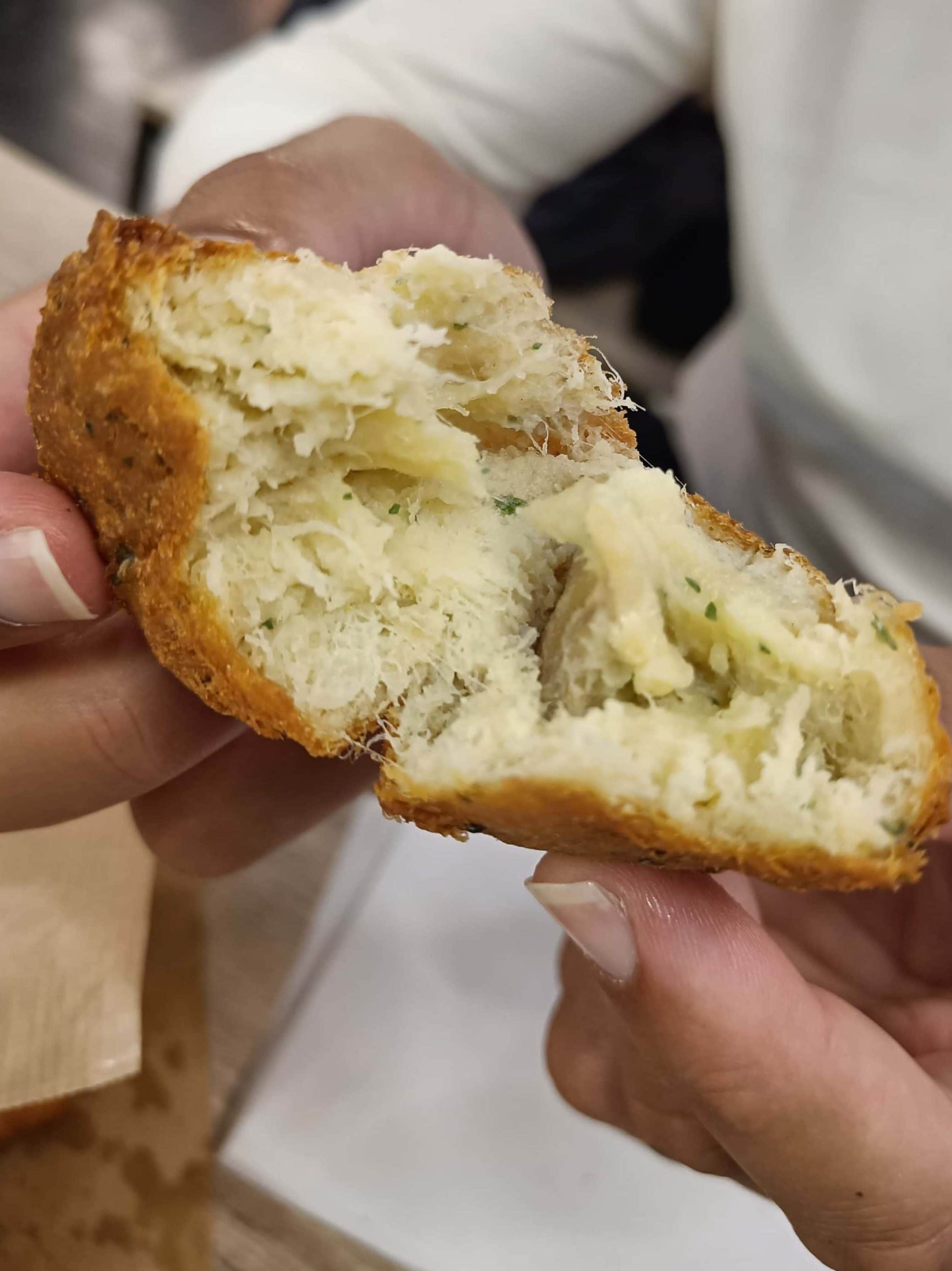 Person holding a torn piece of fluffy bread roll with a savoury filling, over a table—an irresistible taste of the best food Porto has to offer.
