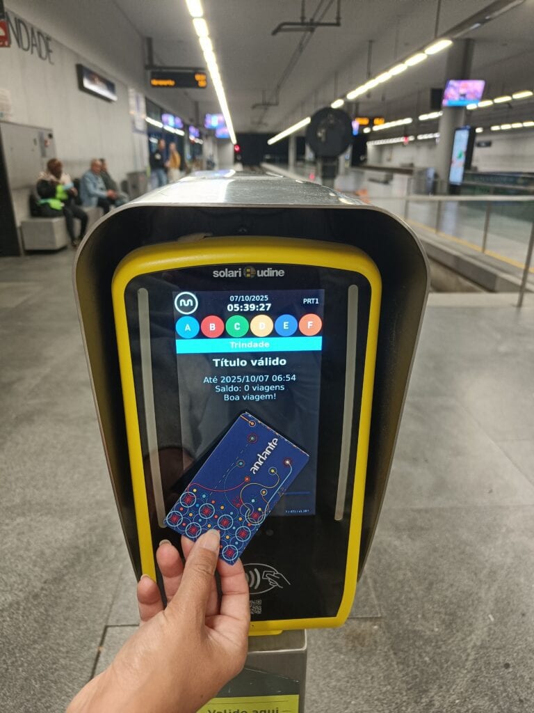 A hand holds a travel card to a ticket validator at an empty underground station platform, capturing a simple moment of getting around Porto.