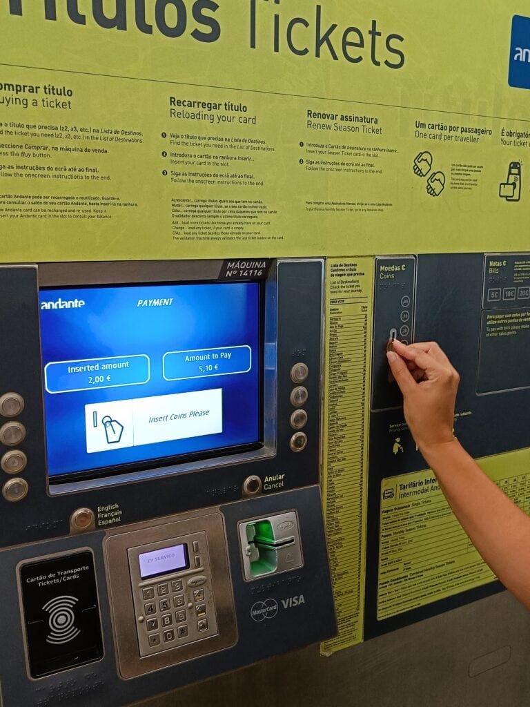 A person inserts a coin into a ticket machine displaying a €7.00 payment screen, an essential step for getting around Porto efficiently.
