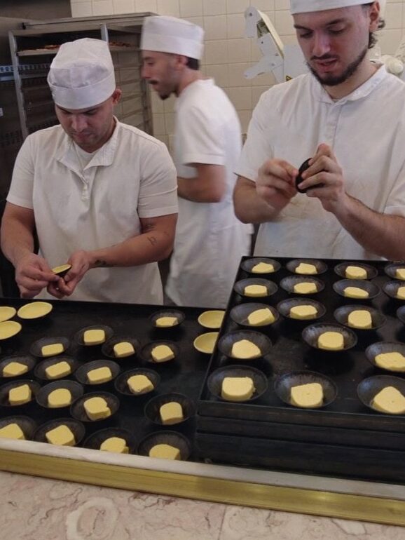 Bakers in white uniforms prepare butter tarts on a baking tray.