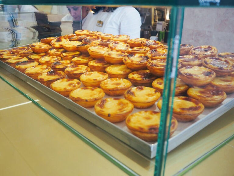 A tray filled with many Portuguese custard tarts, said to be the best pastéis de nata in Porto, on display behind glass at a bakery counter.