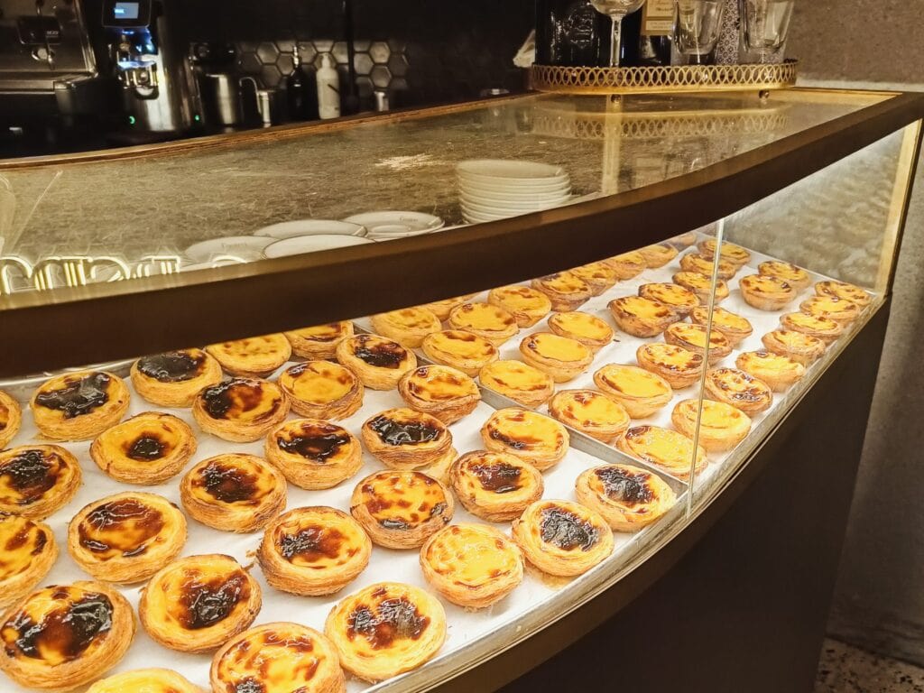 A bakery display filled with rows of Portuguese egg tarts under a glass counter, showcasing some of the best food Porto has to offer.