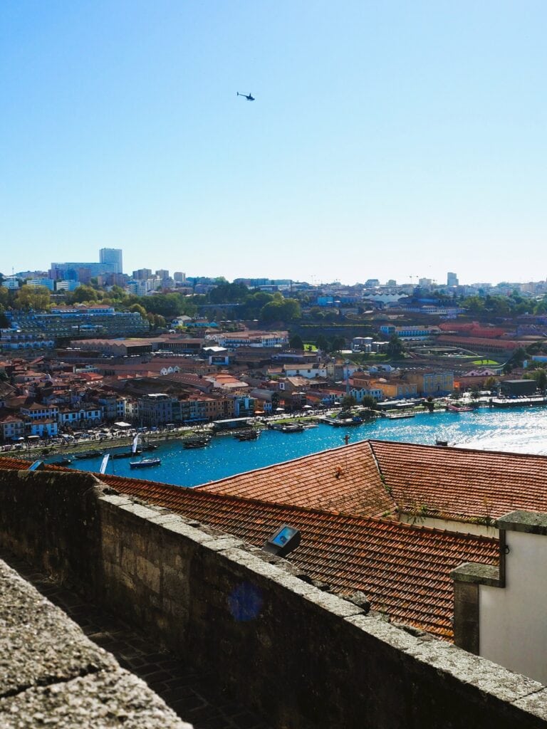 View of a cityscape with red rooftops, blue river, and a helicopter flying in a clear sky above—discover popular attractions in Porto from this breathtaking vantage point.