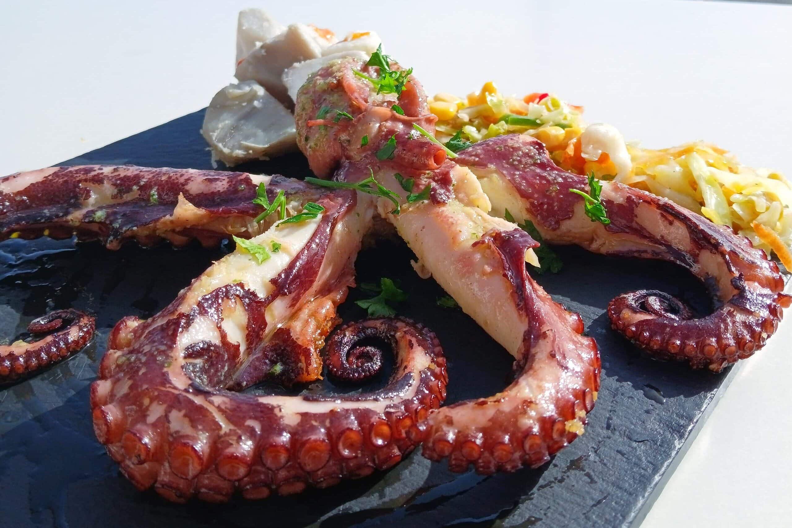 Grilled octopus tentacles garnished with herbs, served on a black slate platter with a seafood salad—a true taste of the best food Porto has to offer.