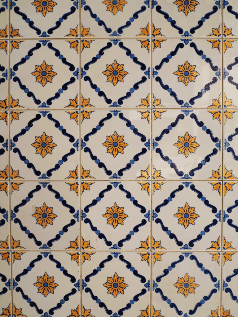 Decorative ceramic tiles with blue and yellow geometric and floral patterns arranged in a repeating grid, reminiscent of the vibrant azulejos found at popular attractions in Porto.