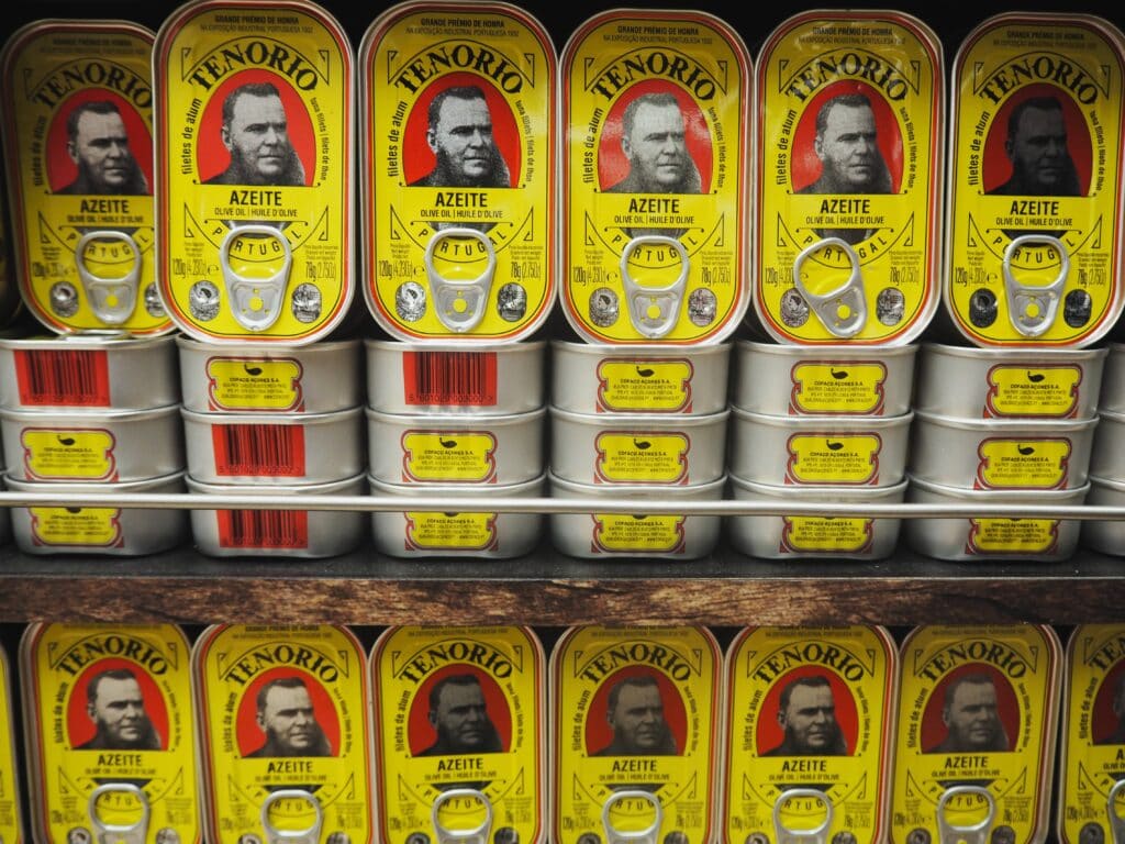 Stacked tins of Tenorio sardines in yellow packaging with a man's portrait and red label, displayed on shelves—an iconic choice among the best food Porto has to offer.