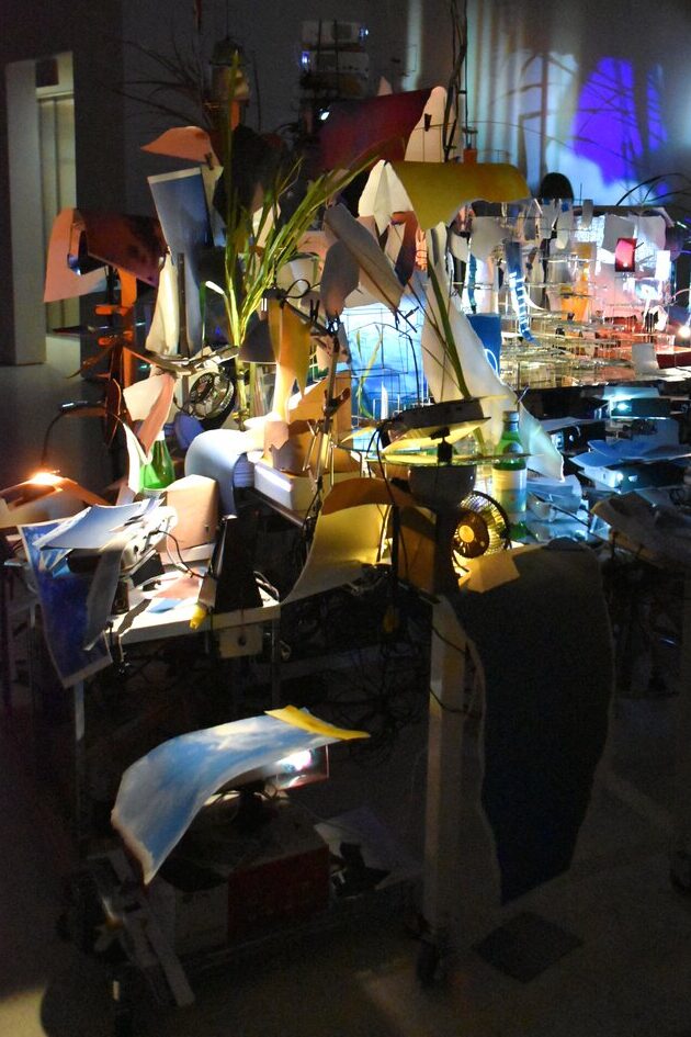 A dimly lit room reminiscent of the Guggenheim Museum in New York, with abstract art adorning the walls, colorful lights casting playful shadows, and plants thriving on cluttered tables.
