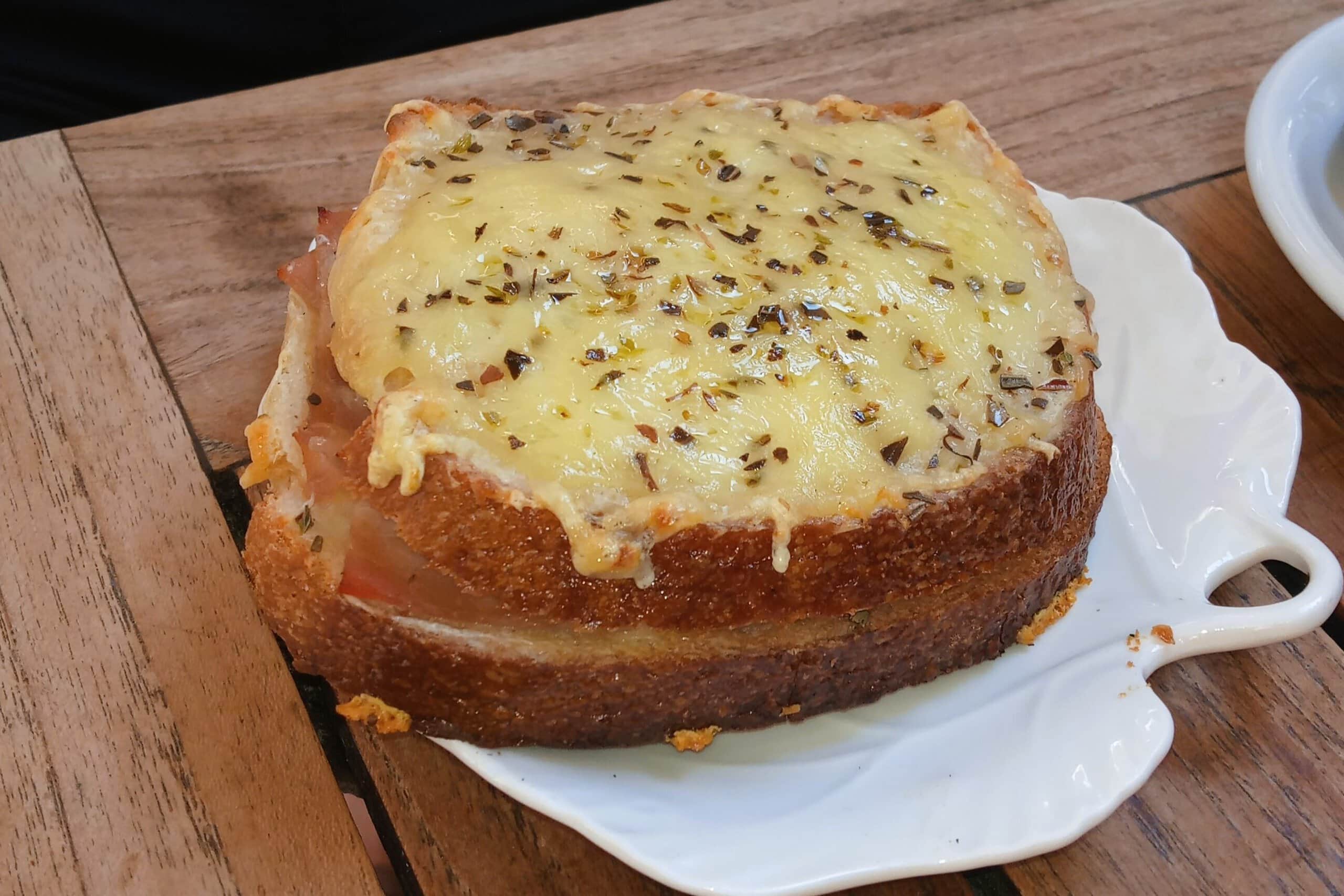 A slice of toasted bread topped with melted cheese and herbs on a white leaf-shaped plate—an irresistible bite and one of the 5x Must-try French Food delights.