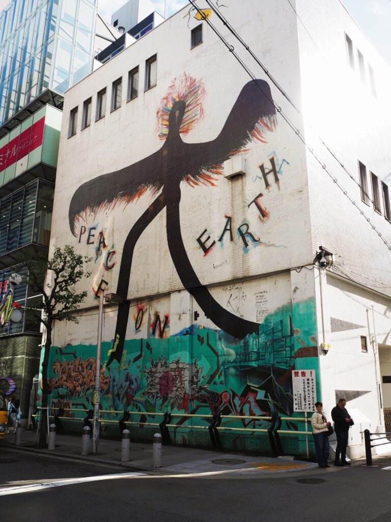 A mural on a city building shows a black figure with “PEACE ON EARTH” and colourful graffiti below.